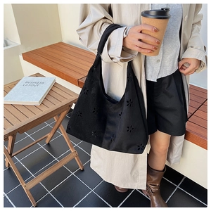 Detail of laser-cut flower pattern on black matte tote bag in casual outdoor setting
