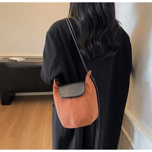 Détail d'un sac seau en daim marron avec bandoulière noire porté sur un manteau noir long