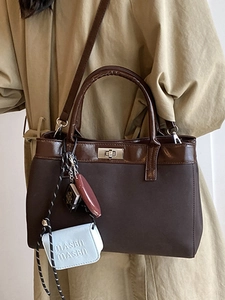 Brown fabric tote bag with leather trim and decorative charms worn with a khaki trench coat