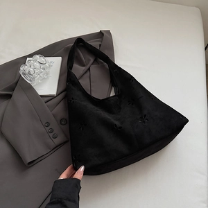 Detail of black suede tote bag featuring laser-cut floral patterns and sleek shoulder strap