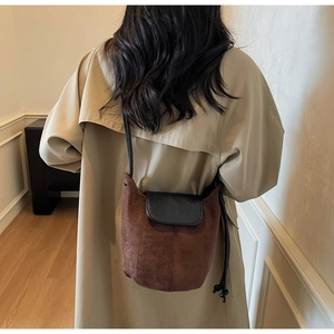 Détail d'un sac seau vintage en daim marron avec rabat en cuir noir porté sur un manteau
