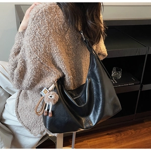 Close-up of black leather tote bag with brown plush pendant on a wide shoulder strap