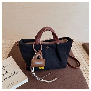 Détail d'un sac à main en daim noir avec poignée marron et charm miniature