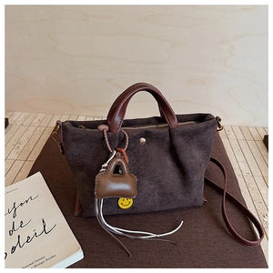Detail d'un sac a main en daim marron fonce avec poignees en cuir et charme smiley