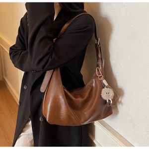 Side view of vintage brown leather tote bag with a cute plush charm on a shoulder strap