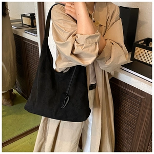 Gros plan d'un grand sac cabas hobo en daim noir porté à l'épaule pour un look minimaliste