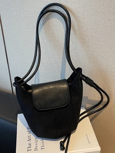 Sac seau noir minimaliste avec textures en daim et cuir lisse sur un livre