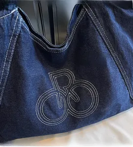 Close-up of dark blue denim tote bag featuring white contrast stitching and embroidered logo