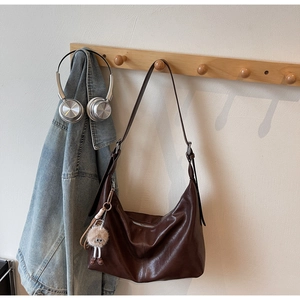 Detail of soft brown leather tote bag with silver buckle and plush charm on wood hanger