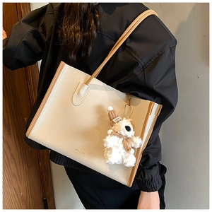 Detail of off-white tote bag with brown trim and a cute teddy bear charm hanging on the side