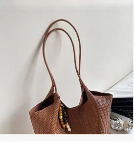 Detail of a brown woven tote bag with slim straps and decorative wooden beads