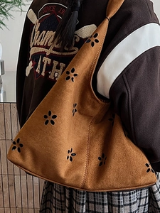 Brown suede tote bag with laser-cut floral patterns shown in a stylish side-carry view
