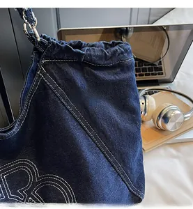 Detailed view of the contrast white stitching and embroidery on dark blue denim tote bag