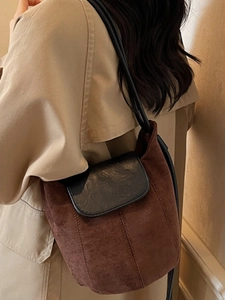 Sac seau minimaliste en daim marron et cuir noir porté avec un trench-coat beige classique