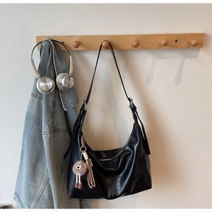 Detail of a large black soft leather hobo bag with a plush charm and tassel accent