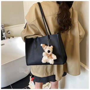 Detail of black pebbled leather tote bag with a white plush bear charm on a model's shoulder