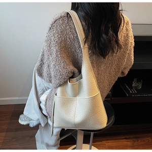 Detailed side view of off-white lychee grain leather hobo bag worn by model indoors