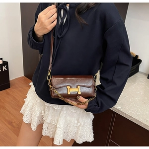 Détail du sac bandoulière marron brillant avec boucle H dorée et décoration de chaîne