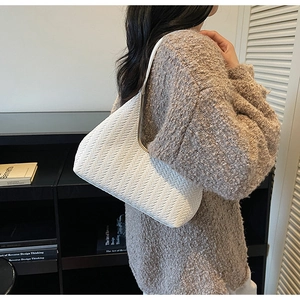 Vue latérale d'un modèle portant un sac sous le bras tressé blanc au style minimaliste