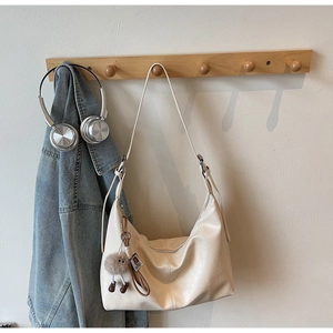 Close-up of creamy faux leather hobo tote bag featuring a cute plush doll charm