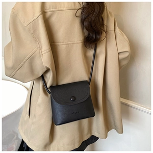 Detail of black pebbled leather texture and embossed logo on minimalist crossbody bag