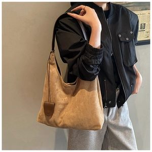 Détail du sac hobo en daim marron avec fine bandoulière et pendentif rond en cuir assorti