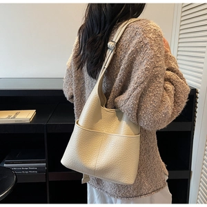 Detail of creamy white faux leather bucket bag showing saddle shape and twin pockets