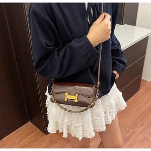 Détail du sac en cuir brillant marron foncé avec boucle H dorée et bandoulière chaîne