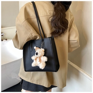 Detailed shot of a black pebbled leather tote bag with a cute white plush bear charm