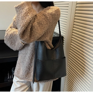 Close-up of a black lychee texture leather hobo bag with two front pockets worn on shoulder