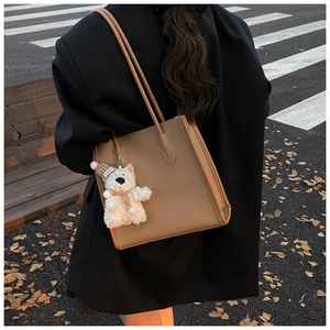 Outdoor shot of a khaki pebble leather tote bag with a cute plush bear charm