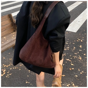 Détail d'un grand sac cabas en daim marron foncé porté par un mannequin en décor d'automne