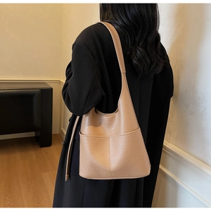 Close-up of pebble grain camel leather bucket bag worn with a black wool coat