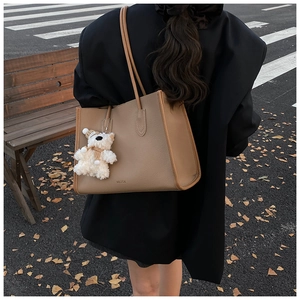 Detail of khaki tote bag with plush bear charm worn with a black blazer on a street