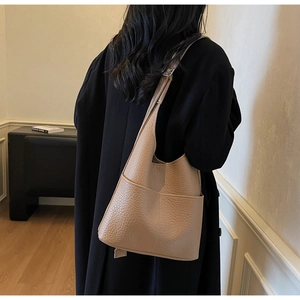 Detail of khaki leather bucket bag showing pebble texture and front slip pocket on shoulder