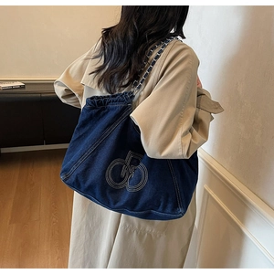Close-up of deep blue denim tote bag featuring embroidered logo and metal chain strap detail