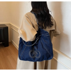 Detail of blue denim tote bag with chain strap and embroidered logo on model shoulder