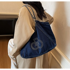 Detail of dark blue denim tote bag with white embroidery and chain woven shoulder strap