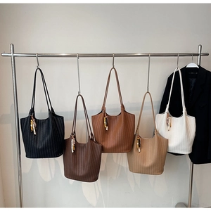 Close-up of woven tote bags in five colors hanging on a rack with beaded charms