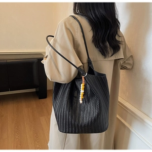 Detail of a large black woven tote bag with a colorful bead charm on a beige coat