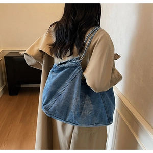 Detail of blue denim tote bag with white contrast stitching and silver metal chain strap