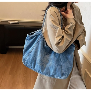 Detail of blue denim tote bag with white embroidery logo and chain strap on shoulder