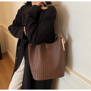 Detail of a dark brown woven leather tote bag with unique ethnic wooden bead pendant
