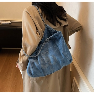 Detail of blue denim tote bag featuring white RB embroidery and chain woven strap