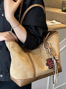 Borsa tote kaki minimalista con ciondolo a forma di orso e nappa mostrata su modella all'aperto
