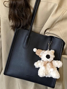 Minimalist black lychee leather tote bag with a cute plush bear charm for daily commuting