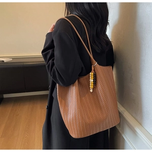 Detail of a brown woven tote bag with beaded charm accessory shown on model's shoulder