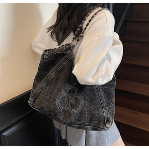 Detail of grey denim tote bag showing chain strap and white embroidery logo on model