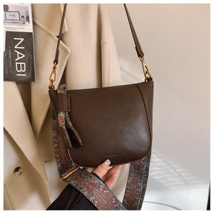 Brown leather saddle bag with wide ethnic pattern strap styled on beige wool coat