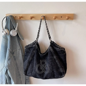 Detail of black washed denim tote bag with chain strap and white embroidery art